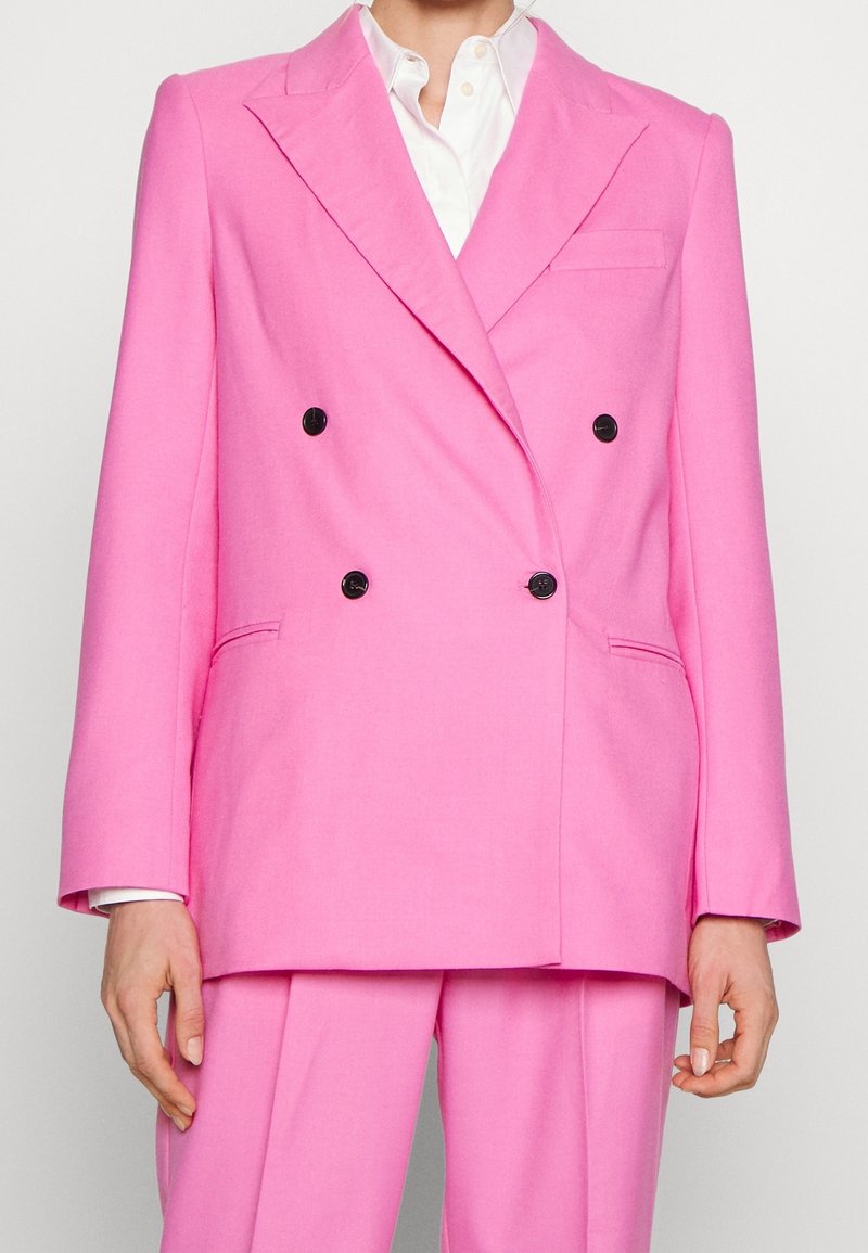 Blazer rosa doppiopetto con bottoni neri, rever a toppa e vestibilità tailored. Include una tasca sul petto e tasche laterali.