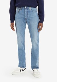 Vaqueros azul claro de corte recto, tela de mezclilla, con cinco bolsillos y cierre de cremallera. Combinados con zapatillas blancas con detalles en negro.