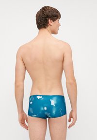 Calções de banho azuis com uma textura suave e brilhante, apresentando vários logótipos e padrões da Nike em tons mais claros por toda a peça.