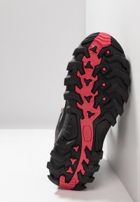 Black and pink hiking shoe sole with deep treads, featuring a textured surface and unique rubber patterns for traction and durability.