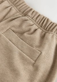 Beige fleece shorts featuring a soft texture, elastic waistband, and a single rear pocket with a flat finish.