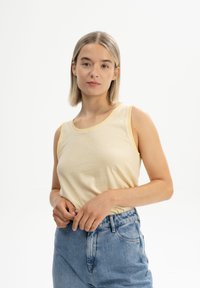 Geel en wit gestreepte mouwloze top met een ronde halslijn, gecombineerd met hooggerimpelde blauwe spijkerbroek. Eenvoudig, casual ontwerp.