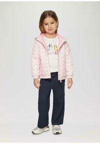 Lichtroze gewatteerde jas met capuchon, gecombineerd met een witte grafische sweatshirt en marineblauwe cargobroek. Sneakers hebben een mix van wit en grijs.