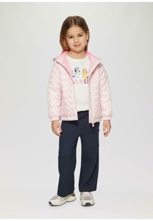 Helles rosa, gesteppte Jacke mit Kapuze, kombiniert mit einem weißen Grafik-Sweatshirt und marineblauen Cargo-Hosen. Die Sneaker weisen eine Mischung aus Weiß und Grau auf.