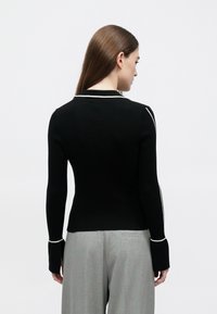 Camisola preta canelada com design ajustado, com remate em branco ao longo da gola e das mangas. Mangas compridas com punhos alargados.