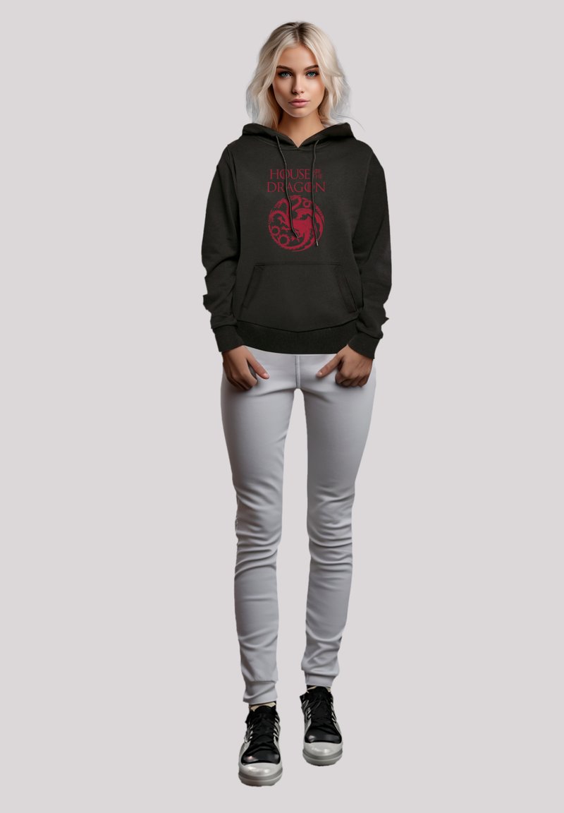 Schwarzer Hoodie mit rotem "House of the Dragon" Grafik auf der Vorderseite, Kängurutasche, verstellbare Kapuze mit Schnürzug, kombiniert mit hellgrauen Hosen und schwarzen Schuhen.