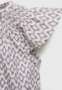 Bloemrijk patroon top met een smocked halslijn. De stof heeft een grijs en wit ontwerp met gele accenten. Korte, gerimpelde mouwen.