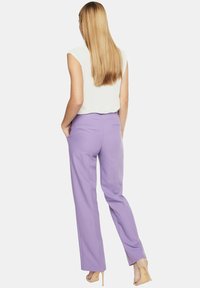 Liliowe spodni z prostym krojem i tylnymi kieszeniami, zestawione z białą topem bez rękawów, model zwrócony tyłem. Gładka faktura materiału.