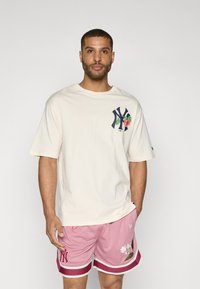 Cream cotton t-shirt with a colorful graphic on the chest, paired with pink mesh shorts featuring floral design and contrasting trim.