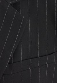 Tissu noir à fines rayures verticales blanches, avec un revers plié et un détail de couture horizontal.