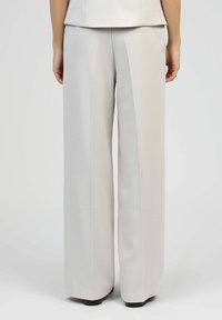 Pantalons larges en tissu gris clair; texture lisse avec des plis à l'avant; l'ourlet touche le sol, assortis à un haut correspondant.