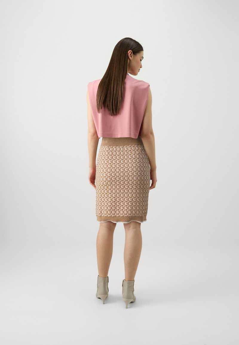 Gekürztes pinkes Oberteil und beige knielange Rock mit strukturiertem Muster, abgeschlossen mit einer gewellten Kante. Model trägt hellfarbene Knöchelstiefel.