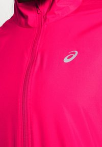 Helles pinkes Jackett mit Reißverschluss, hohem Kragen und einem dezenten silbernen Logo. Glatte Textur und körpernahe Passform für aktive Nutzung.