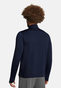 Marineblå langærmet atletisk top med høj krave og struktureret stof. Har flade sømme og en tætsiddende pasform, der er velegnet til aktivt tøj.