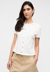 Λευκό πουκάμισο με κοντά μανίκια και στρογγυλή λαιμόκοψη με κλείσιμο χρυσών κουμπιών, που διαθέτει εφαρμοστή σχεδίαση και απαλό, λείο ύφασμα.