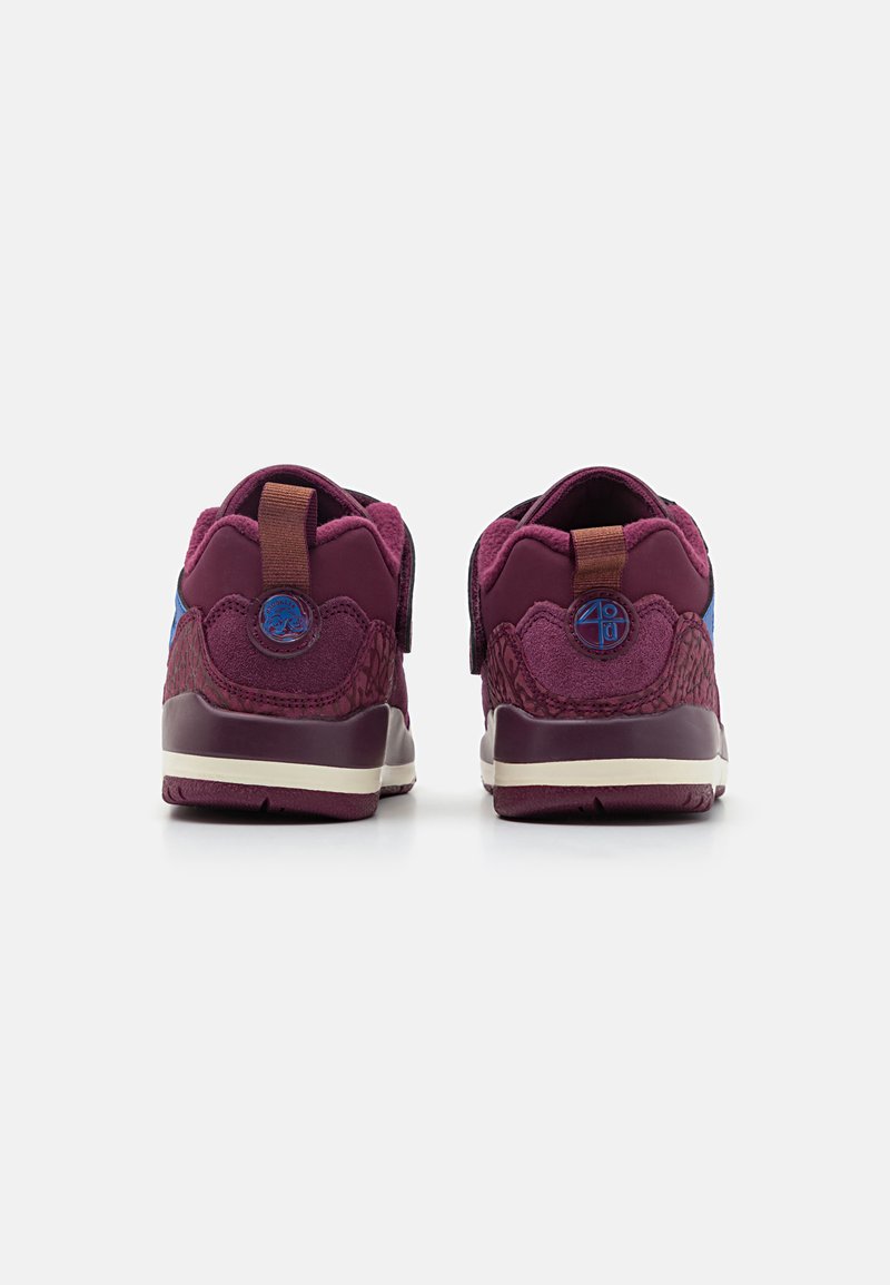 Las zapatillas deportivas moradas presentan un diseño texturizado, un collar acolchado, acentos azules y un tirador en el talón. La suela es de color marfil.