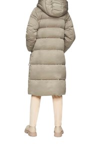 Beige gewatteerde jas met een capuchon, met horizontale stiksels en een middellange pasvorm. Gecombineerd met lichtgekleurde broek en casual schoeisel.