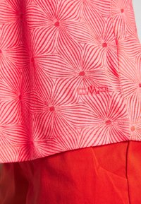 Camisa rosa con un patrón geométrico circular en un rosa más claro, que presenta el logo "CMRL" bordado en una esquina. Combinada con pantalones rojos.