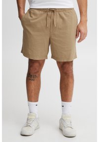 Beige textured shorts with an elastic waistband and drawstring. White crew socks and white sneakers complete the outfit.