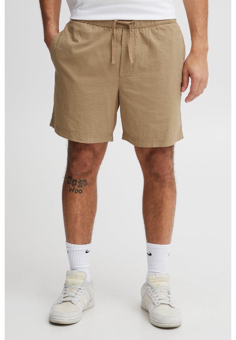 Beige textured shorts with an elastic waistband and drawstring. White crew socks and white sneakers complete the outfit.