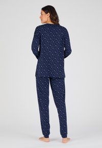Marineblauw pyjama-set gemaakt van zachte stof, met witte halve maan patronen. Langdurige mouwen met zijsplitsen; bijpassende broek met elastische taille.