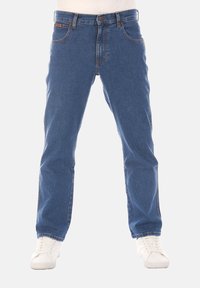 Jeans in denim blu con design a gamba dritta, stile a cinque tasche, cuciture a contrasto e zip, indossati con sneakers bianche.