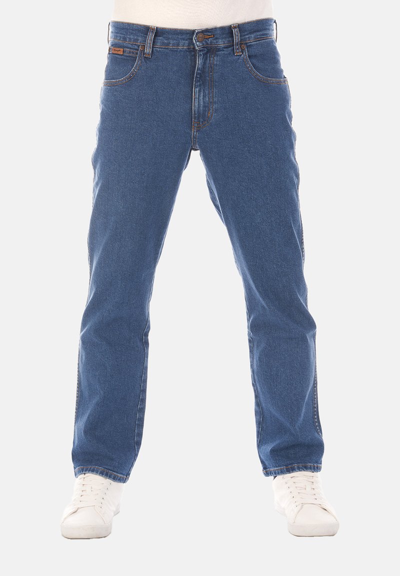 Jeans in denim blu con design a gamba dritta, stile a cinque tasche, cuciture a contrasto e zip, indossati con sneakers bianche.