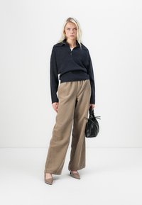 Granatowy sweter polo dzianinowy z kołnierzykiem, w zestawieniu z szerokimi spodniami w kolorze khaki. Akcesoria to czarna torba strukturalna i beżowe szpilki.