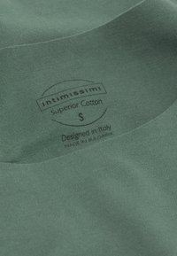 Zelená bavlněná látka s hladkým povrchem, na které je štítek s nápisem "intimissimi," označující velikost S, a údaji o designu a výrobě.