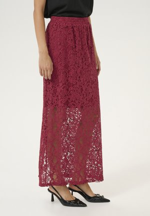 Burgundy lace maxi skirt with an elastic waistband, featuring floral patterns and a partially sheer design, paired with black heeled shoes.