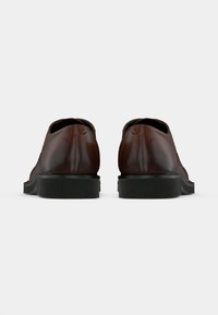 Chaussures en cuir marron avec une texture lisse, un bout arrondi et une semelle en caoutchouc noire, présentant des détails de couture minimalistes à l'arrière.