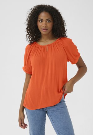 Blouse orange à manches courtes avec un col froncé et un petit détail en forme de trou à l'avant, fabriquée à partir d'un tissu texturé léger.