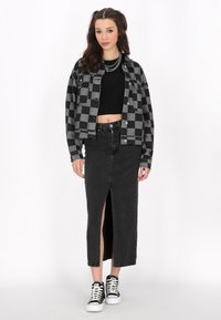 Svart och grå rutigt denimjacka över en svart crop top, kombinerad med en svart högslitskjol och högstövlar.