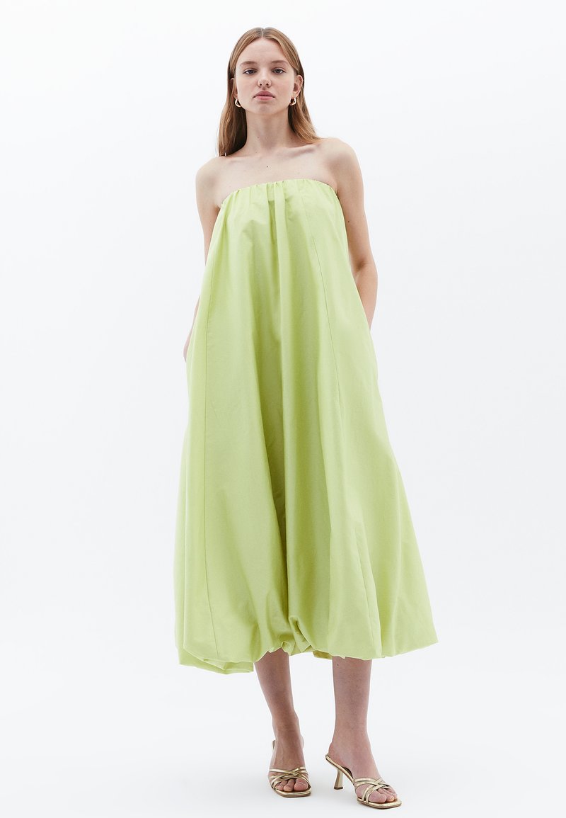 Trägerloses, leichtes Kleid aus hellgrünem Stoff. Verfügt über eine lockere, ballonartige Form und seitliche Taschen. Einfache, glatte Textur.