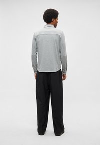 Camisola cinzenta de manga comprida com bainha curva e punhos com botões, combinada com calças largas pretas. O tecido parece macio e texturizado.