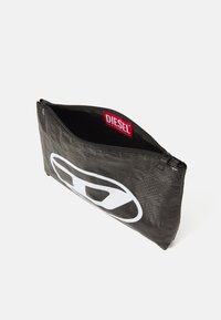 Borsa nera con zip realizzata in materiale testurizzato, con un grande logo bianco Diesel su un lato e un'etichetta rossa del marchio all'interno.