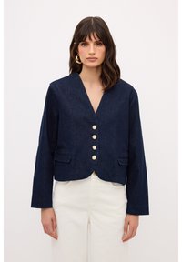 Chaqueta de mezclilla azul marino recortada con escote en V, cinco botones parecidos a perlas, dos bolsillos delanteros y mangas largas. Textura suave y diseño estructurado.