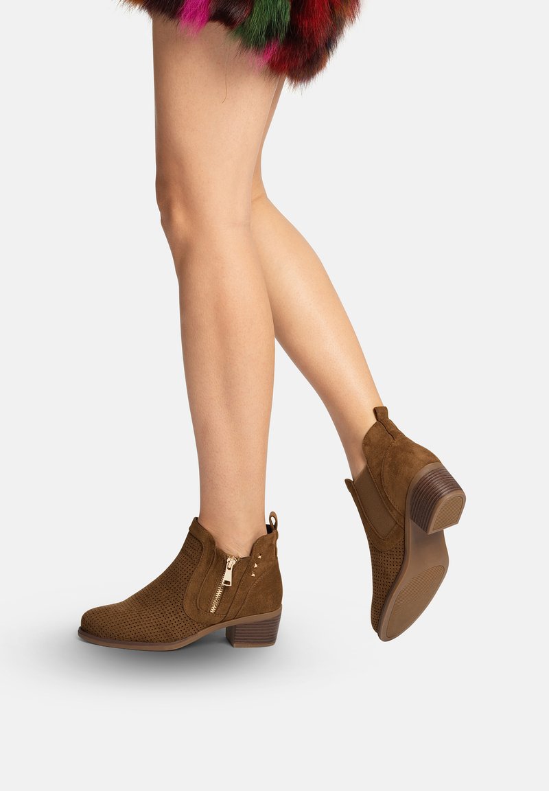 Ben iført brune ruskindsankelstøvler med perforeret design, sidelukning med lynlås, lav blokhæl, kombineret med flerfarvet pelskørt synligt øverst.