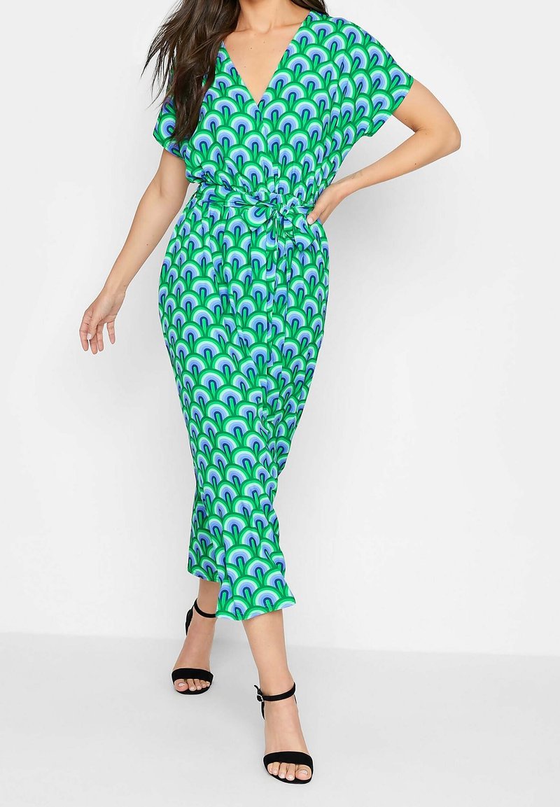 Robe verte avec motif arc-en-ciel bleu et sarcelle, encolure en V, manches courtes, taille élastique et ourlet à la cheville, associée à des talons noirs.