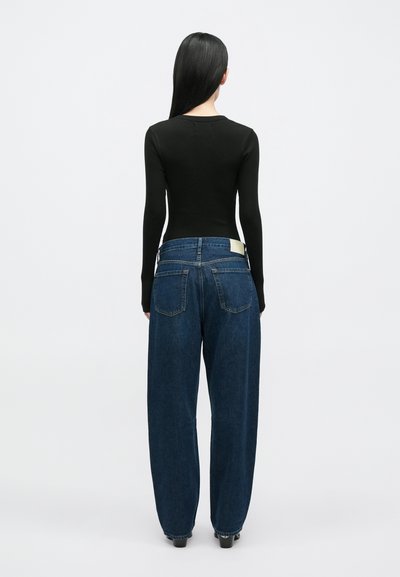 Fekete bordázott hosszú ujjú felső laza szabású sötétkék farmernadrággal párosítva. A farmernadrág szabványos öt zsebes kialakítású, és hátul egy címke található rajta.