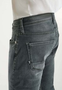 Jeans in denim grigio scuro con vestibilità slim. Le caratteristiche includono tasche posteriori, una vita standard e dettagli di cucitura discreti.