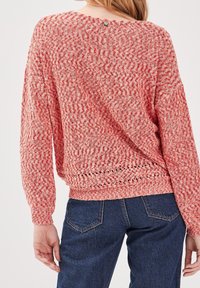 Luźny sweter w czerwono-białe wzory o fakturze dzianiny, z okrągłym dekoltem i guzikami z tyłu. Połączony z dżinsami.