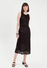 Robe midi noire en dentelle avec un motif en losanges, design sans manches et un ourlet décoratif. Associée à des sandales à talons blocs noires.