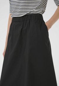 Falda negra a la altura de la rodilla con cintura elástica y bolsillos laterales; hecha de una tela suave y ligera; diseño minimalista.
