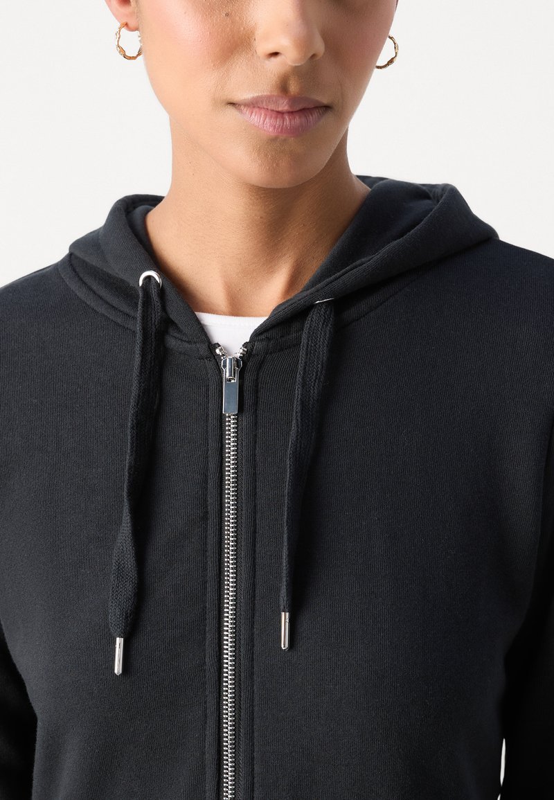 Black zip-up hoodie made of soft fabric. Features a drawstring hood, silver zipper, and ribbed cuffs. Simple design with no patterns.