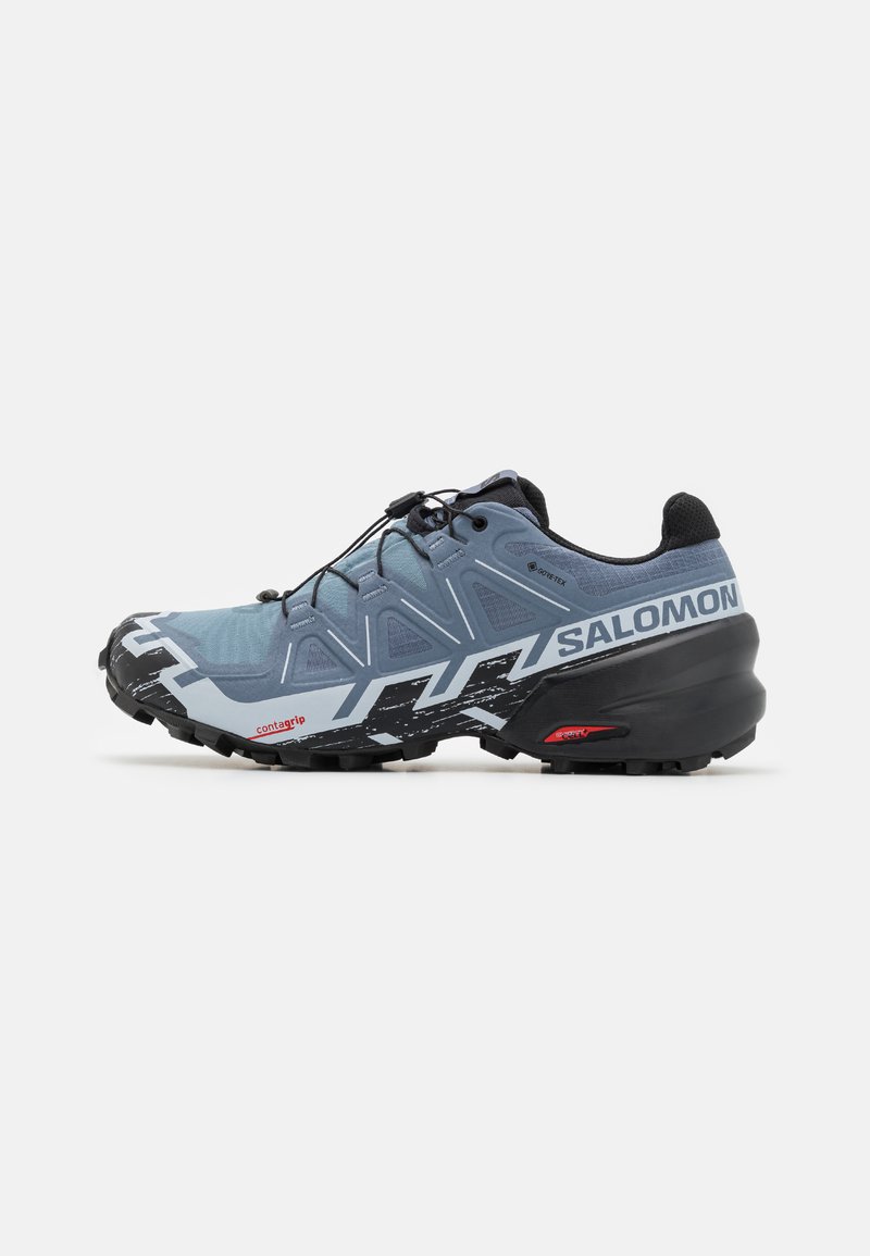 Chaussure de trail running, upper synthétique en bleu clair avec des accents sombres, semelle extérieure en caoutchouc noir, motif de traction unique et système de laçage rapide.