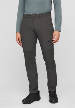 Personne portant un pantalon d'extérieur gris foncé avec des renforts aux genoux, un haut à manches longues vert clair et des chaussures de randonnée noires.