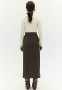 Crèmegekleurde geribbelde trui met knopen op de schouders, gecombineerd met een bruine kokerrok en bruine enkellaarsjes met gespen. Achteraanzicht.