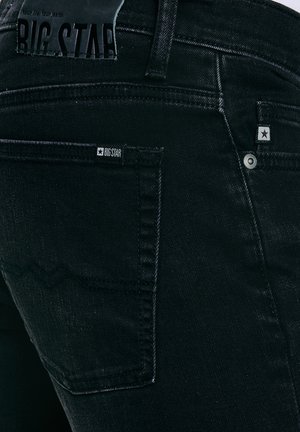 Zwarte spijkerbroek achterzak met Big Star-logo labels en stiksel details in een close-up weergave.