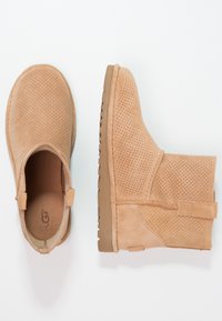 Beżowe zamszowe botki za kostkę z perforowanym wzorem, okrągłym noskiem i gumową podeszwą. Posiadają uchwyt do zakładania oraz subtelne detale w szwie.